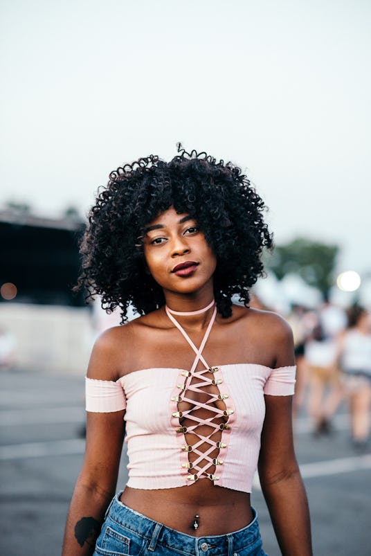 A girl with an afro hairstyle in a light pink top with a tattoo on her right hand