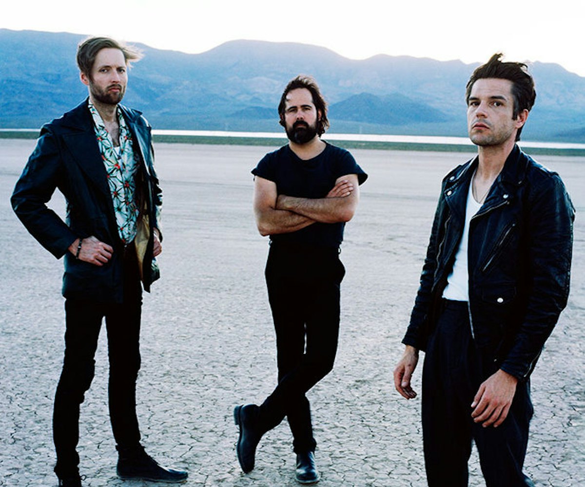 The members of The Killers band standing on a concrete floor in black outfits
