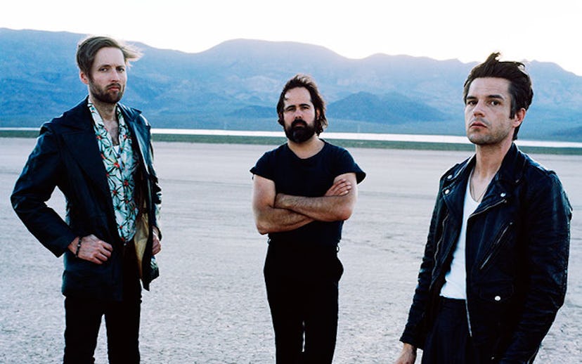 The members of The Killers band standing on a concrete floor in black outfits