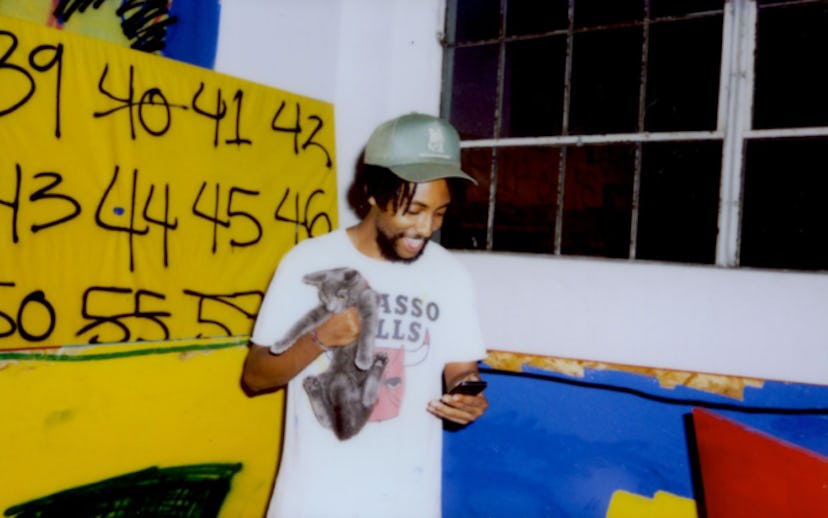 Awol Erizku holding a cat while looking at his phone