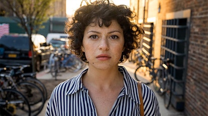 Alia Shawkat walking down a street in a striped shirt in a scene from Search Party 