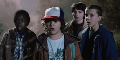 The main cast from Stranger Things in a forest looking at something shocked
