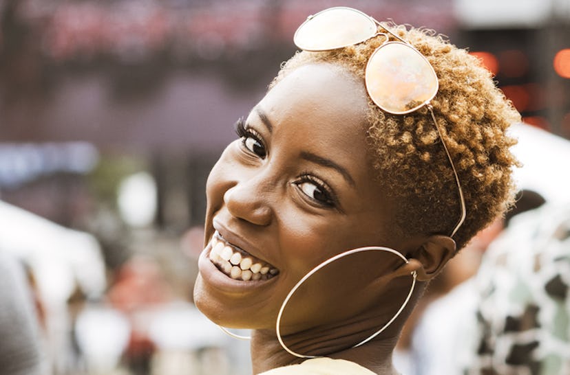 A woman with short hair, large hoop earrings and sunglasses on her head, smiling 