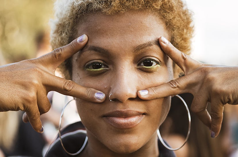 A woman with large hoop earrings and yellow statement eyeliner on her lower eyelid 