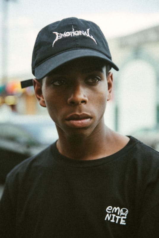 A young man wearing a black cap with a text sign that says "Emotional" and a black t-shirt with an "...