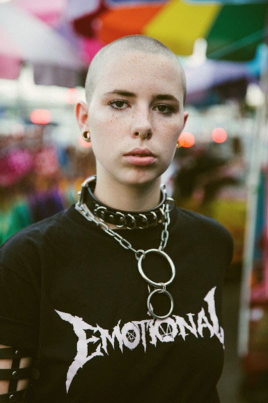 A young bald person with a big choker necklace with chains and a black t-shirt with a text sign that...