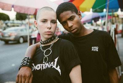 Two people wearing chains and black shirts with "Emotinal" and "Emo Nite" text signs