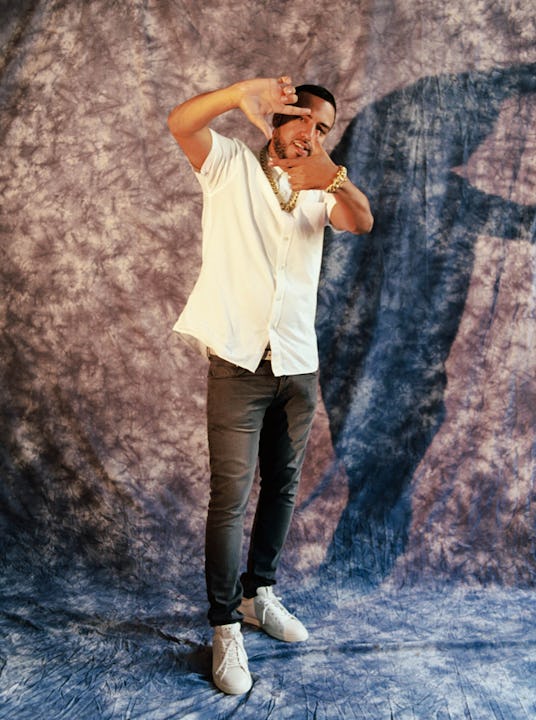 French Montana posing for a photo in a white button down shirt, black pants, white sneakers and gold...