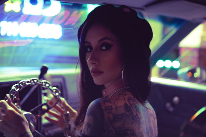 Natasha Lillipore in a black beret at the steering wheel of her ’79 Chevrolet Monte Carlo looking ba...