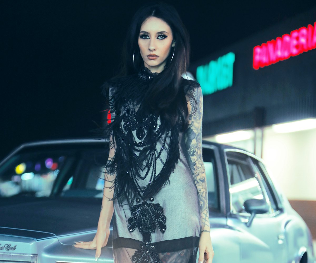 Female tattoo artist Natasha Lillipore wearing a black and gray dress leaned against her car ’79 Che...