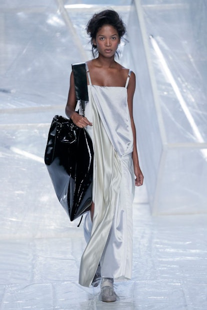 A female model in a gray long dress carying a big black bag