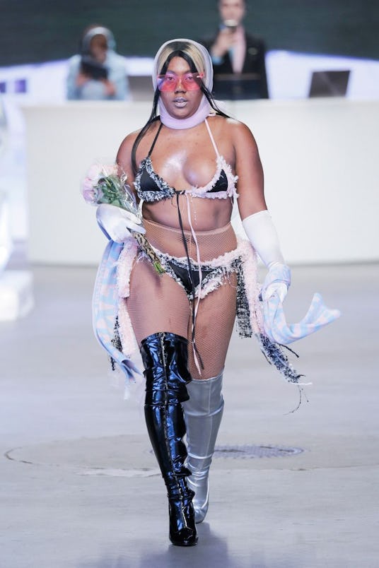 A female model in a tape black and gray bathing suit and matching kneehigh boots, holding flowers