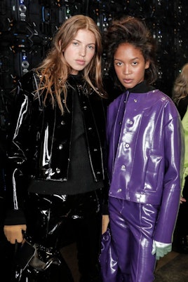 Two models in matching leather pants and jackets, except one is in purple and the other in black 