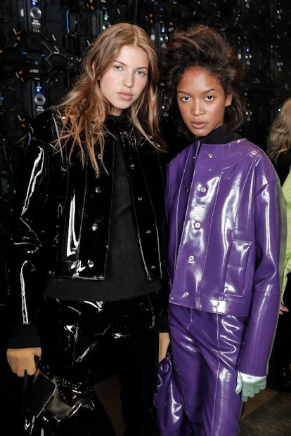Two models in matching leather pants and jackets, except one is in purple and the other in black 