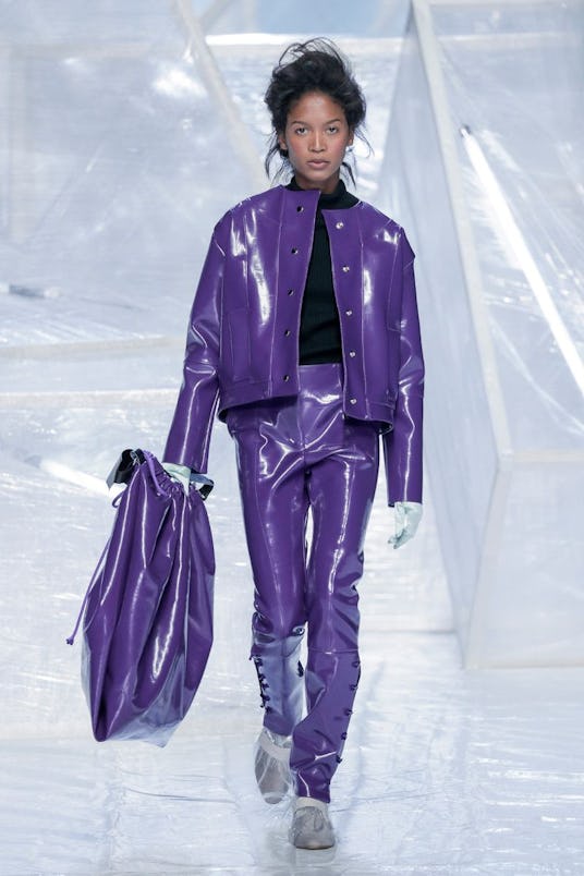 A female model in a leather purple two-piece and a matching bag walking the runway