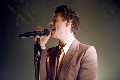 Harry Styles singing in a simple brown-ish suit