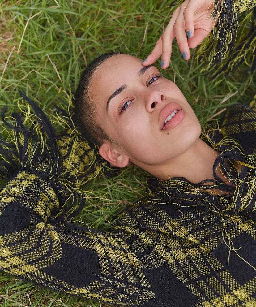 Jorja lying down in the grass in a black and yellow sweatshirt with fringe on the collar