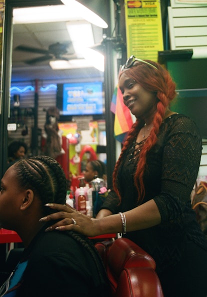 A stylist with red hair in braids, braiding her customer's hair 