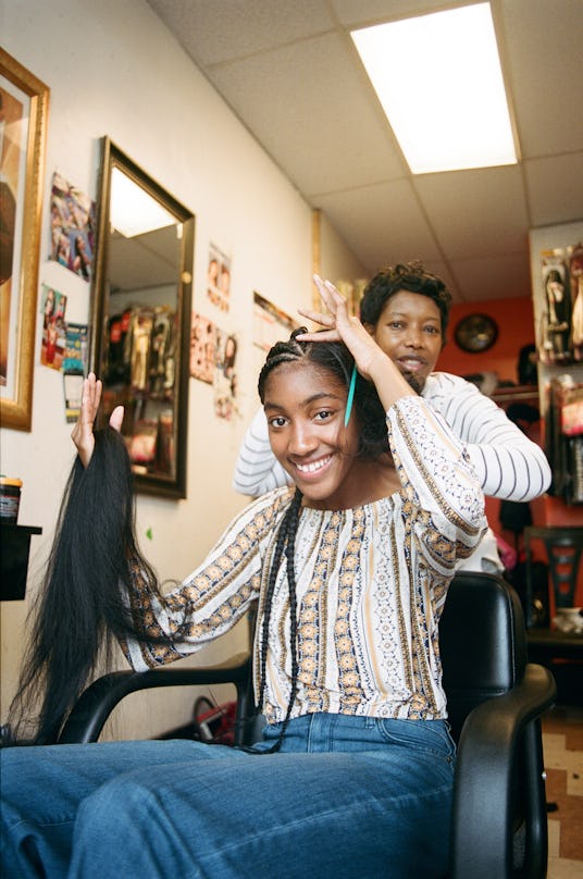 A woman holding hair extensions in her hand as she gets her hair braided 