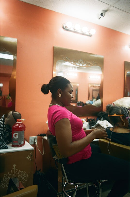 A hair stylist sitting as she braids her customer's hair 