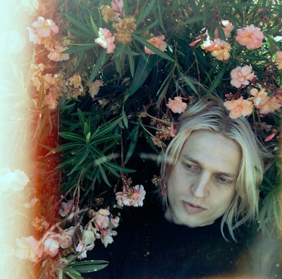 Artist Mosss posing in a field of flowers for a cover of her single “Here If You Want (Pale Blue).”