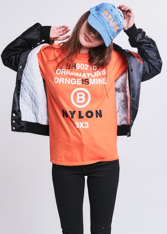 A female model posing while wearing an orange shirt and a light blue cap