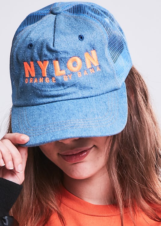 A girl covering her face with a blue cap with a "Nylon" text sign