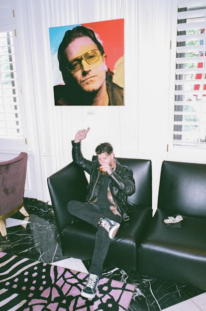 Nathan Williams of the Wavves band sitting with a drink and pointing at Bono Vox's picture