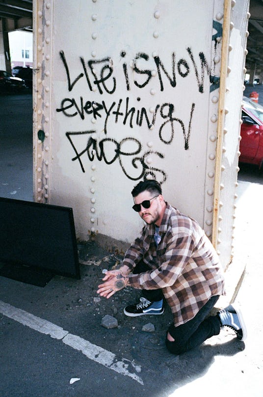 Nathan Williams of the Wavves band squatting next to a "Life is now, everything fades" graffiti