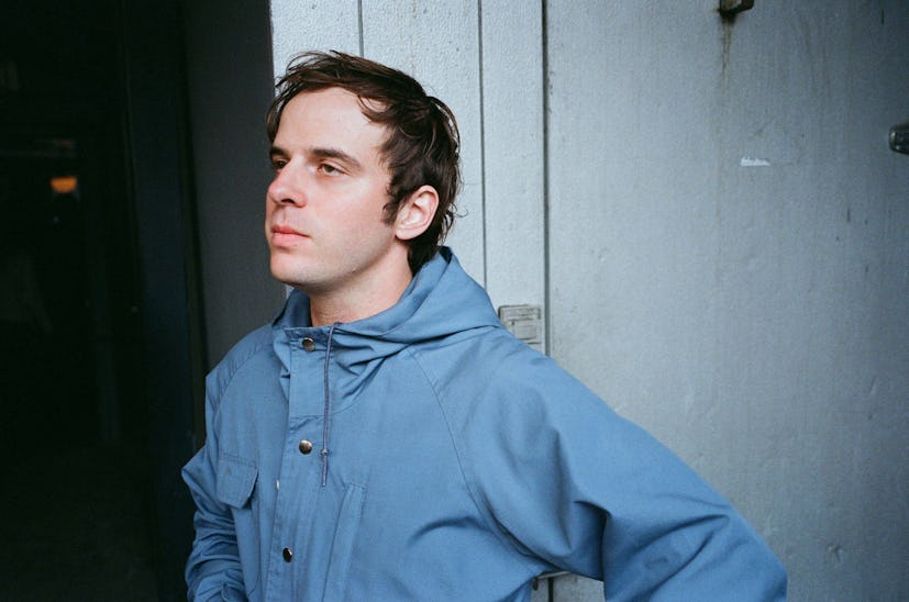 Semi-profile view of Alex Gates of the Wavves band in a blue jacket next to a white wall
