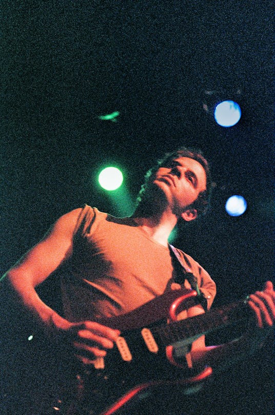 Alex Gates of the Wavves band in a grey top with rolled-up sleeves playing guitar 