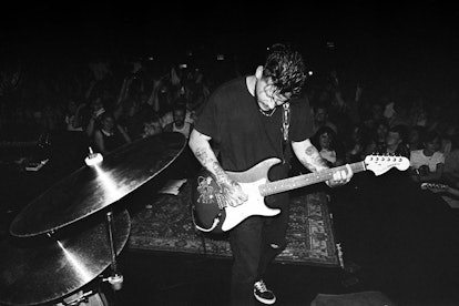 Nathan Williams of the Wavves band playing guitar with a crowd behind him in black and white
