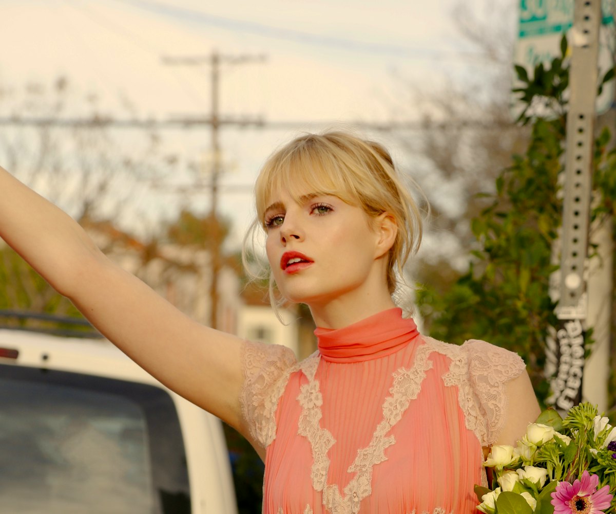 Lucy Boynton wearing a pink and white shirt and holding flowers in a scene from Sing Street 