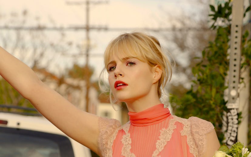 Lucy Boynton wearing a pink and white shirt and holding flowers in a scene from Sing Street