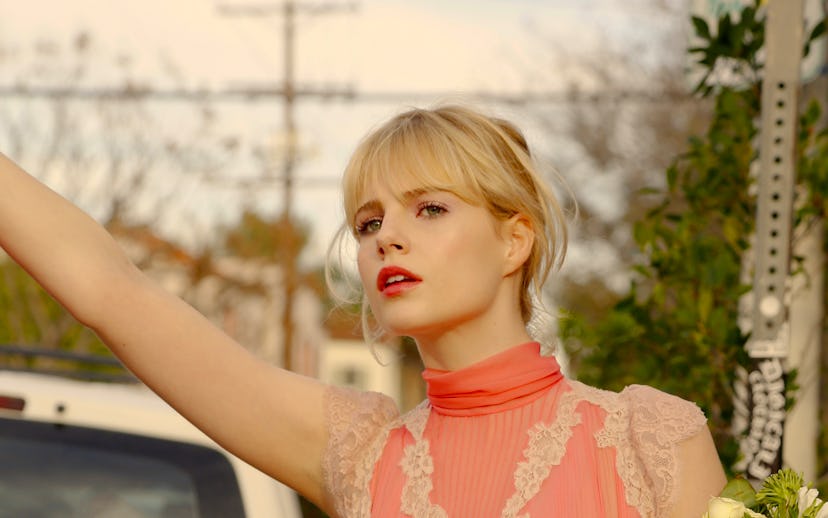 Lucy Boynton wearing a pink and white shirt and holding flowers in a scene from Sing Street 