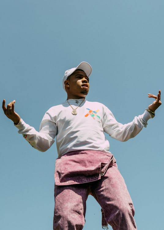 Taylor Bennett wearing a white hoodie and a cap in combination with purple pants and a lot of jewelr...