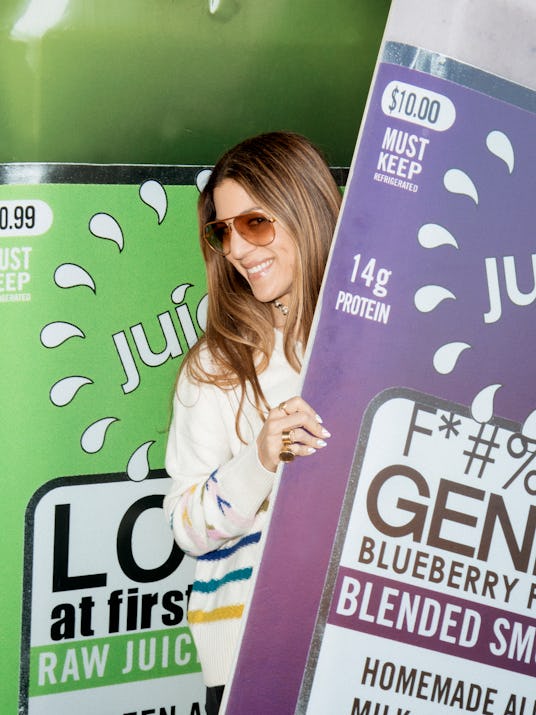 A woman smiling at the photographer while she holds the juice cardboard advertisements
