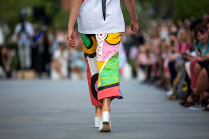 Model in multicolored pants with an abstract print walking on the runway with a crowd looking on