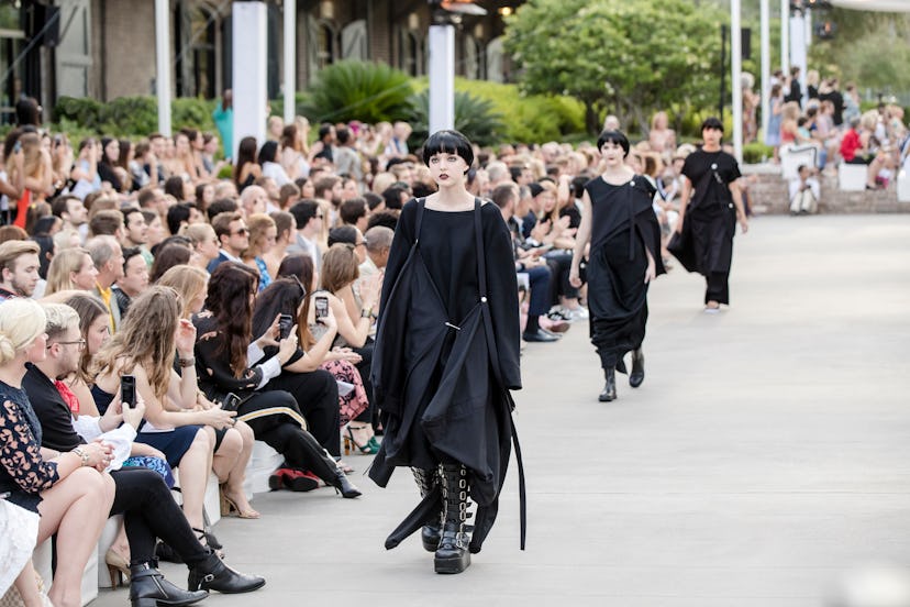 Three models going down the runway in black dresses with a crowd looking on