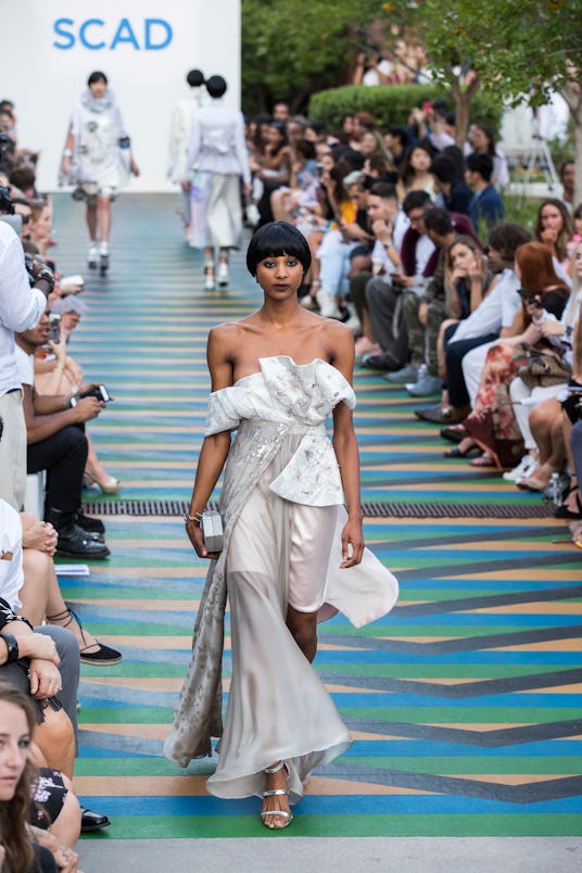 A female model in a silver satin dress going down the runway