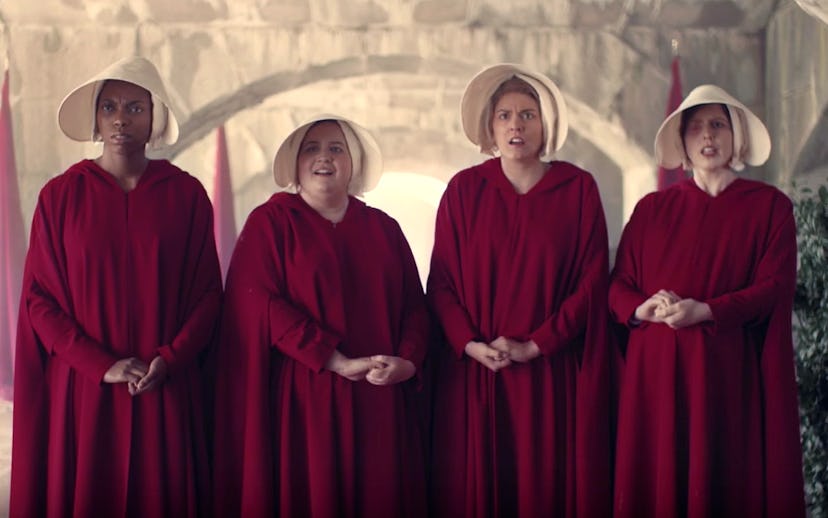 Four ladies standing while wearing long red dresses and white hats with shocked facial expressions