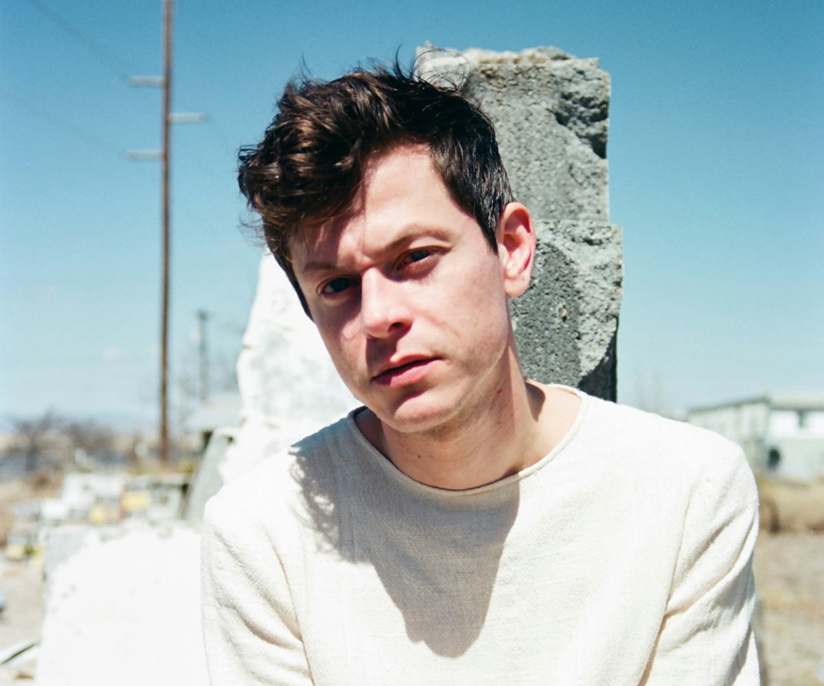 Michael Hadreas in all white crouching in front of a rock in a desert