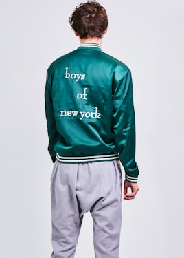 A male model posing in a green bomber jacket with "Boys of New York" text on the back