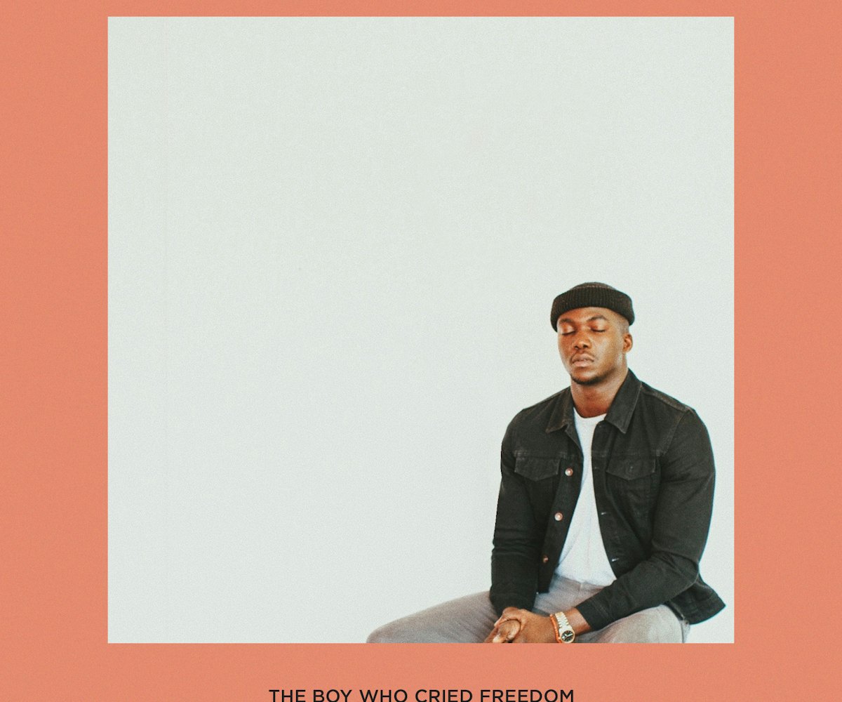 Jacob Banks sitting with closed eyes in a white shirt, black jacket, and grey pants on the cover of ...