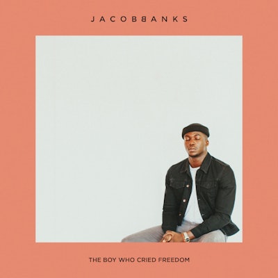 Jacob Banks sitting with closed eyes in a white shirt, black jacket, and grey pants on the cover of ...