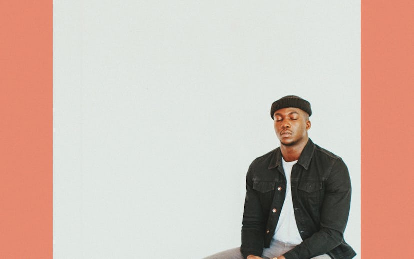 Jacob Banks sitting with closed eyes in a white shirt, black jacket, and grey pants on the cover of ...