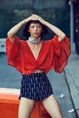A model wearing navy blue shorts and a flowy red crop top with big sleeves