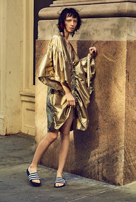 A model wearing a gold dress and striped sandals