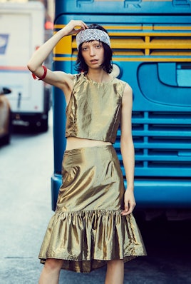 A model wearing a gold knee-length skirt, a gold sleeveless shirt and a white and blue bandana