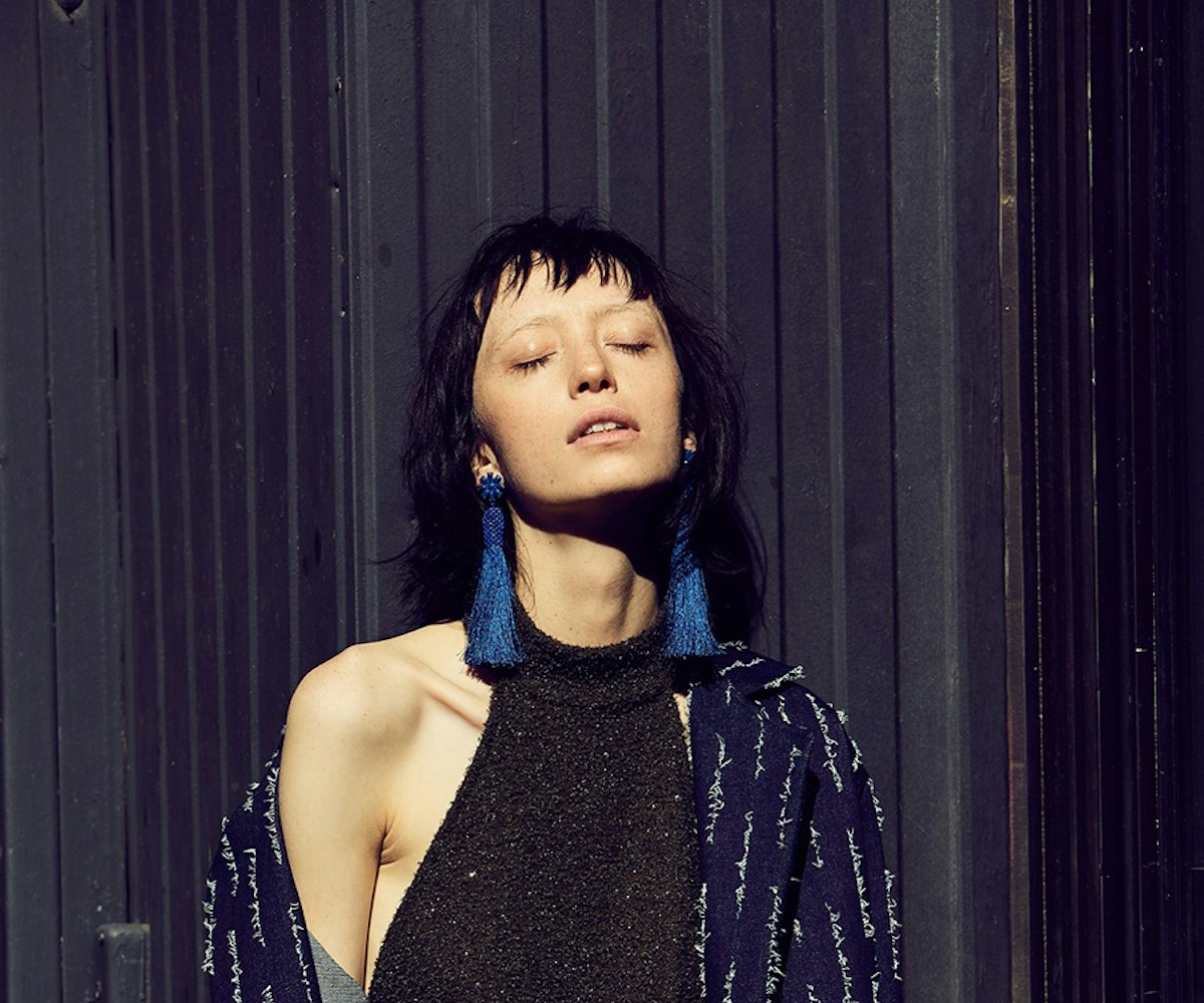 A model posing in a black sleeveless dress, with a navy blue, patterned, long jacket